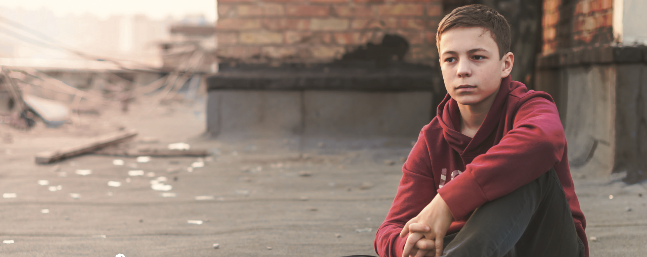 Teenage boy looking serious sitting by an old building