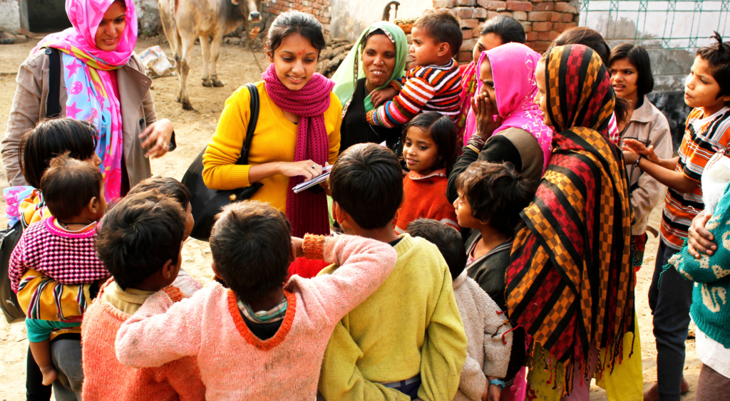 Social Worker in India stands with a group of children in bright clothing talking to her