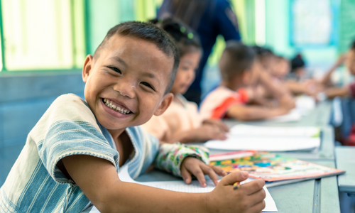 A young Thai child in school with classmates in the background.