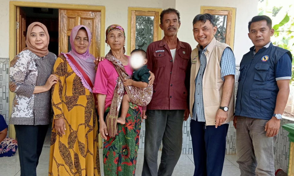 Foster Care family in Indonesia standing together holding a child while being visited by staff from Harum