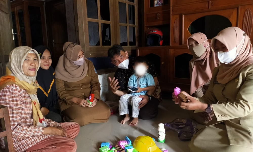 Foster Care Family in Indonesia sitting on the floor during a visit from Harum staff